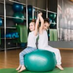 two-little-girl-sitting-back-back-exercising-ball-together